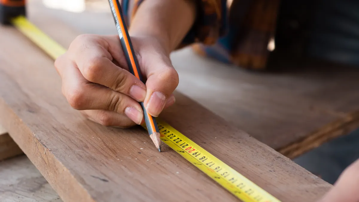 person marking a board while measuring with a tape measure