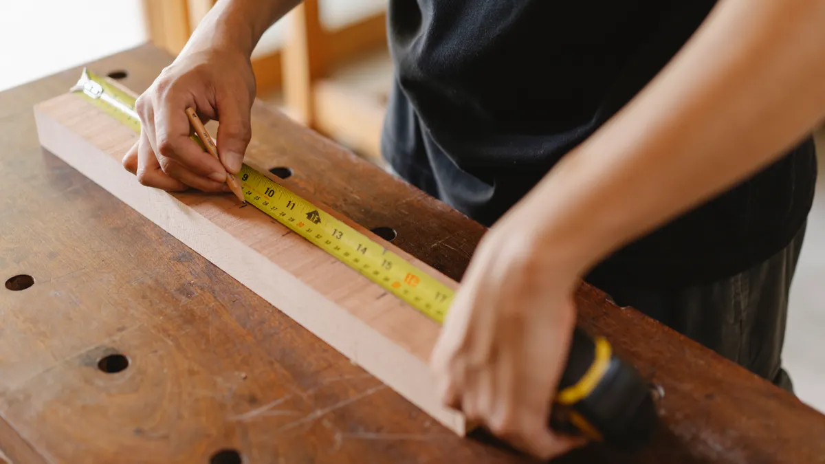 person measuring a board on a workbench with a tape measure