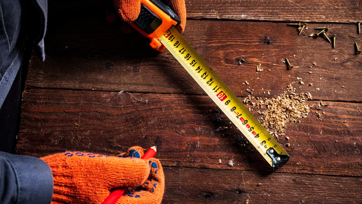 Mulch Conversion Guide: Inches to Cubic Feet, Cubic Yards, and Bags Gloved hands measuring wood with a tape measure