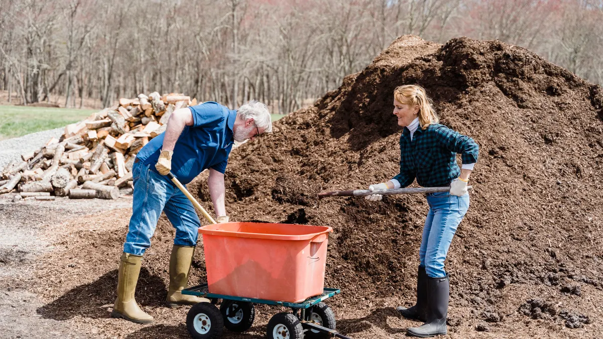 two people shoveling a large pile of mulch